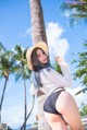 A woman in a white shirt and black shorts leaning against a palm tree.